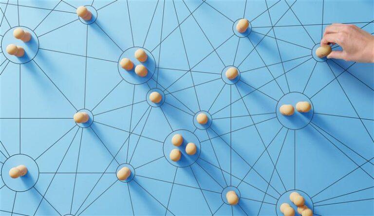 Réseau connecté de nœuds représentés par des pions en bois, manipulé par une main, symbolisant l'automatisation et la redirection des demandes avec un chatbot intégré.