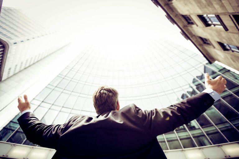 Homme en costume levant les bras devant des gratte-ciel modernes, symbolisant la centralisation et le suivi des opportunités avec Microsoft 365 Sales