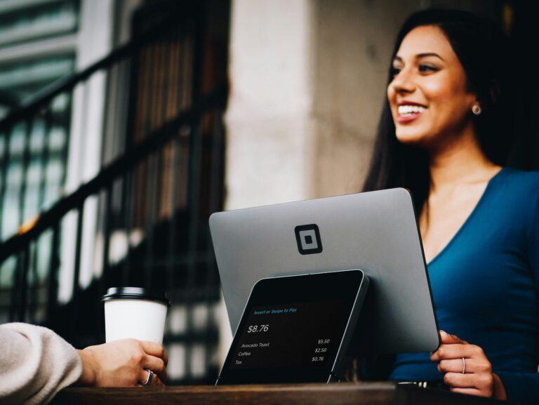 Une femme souriante avec un terminal de paiement, illustrant la fidélisation client grâce à un service personnalisé et rapide.