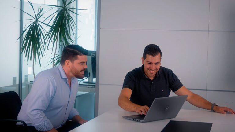 Deux hommes souriants collaborant sur un ordinateur portable, découvrant les fonctionnalités de Microsoft Copilot pour améliorer leur productivité.